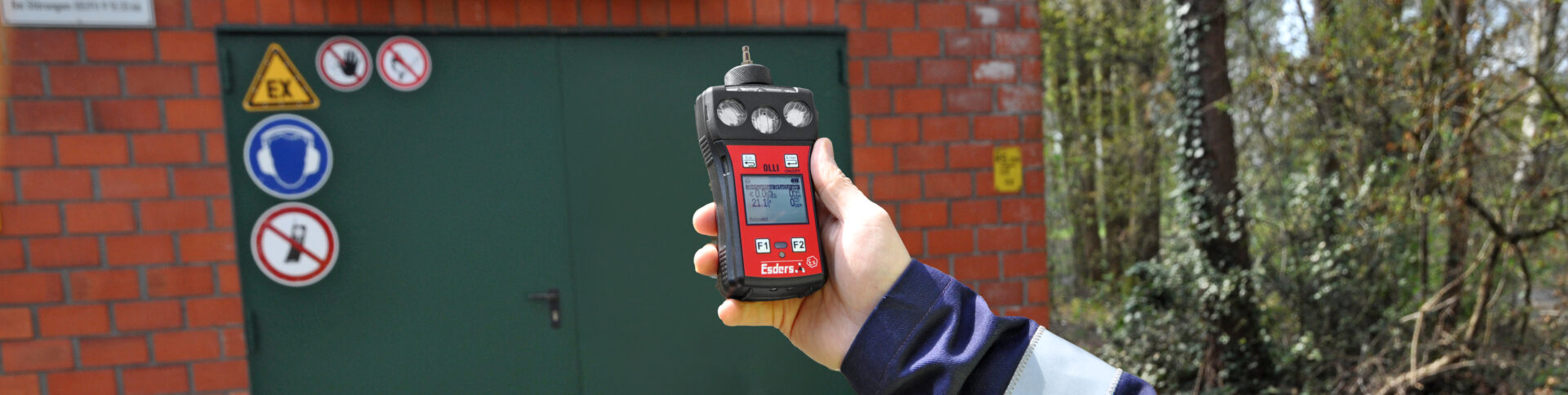 OLLI Gasdetektor beim Freimessen in einer Hand eines fachkundigen Mitarbeiters vor einem GasReglerhäuschen in Deutschland. Drumherum stehen ein paar Bäume.